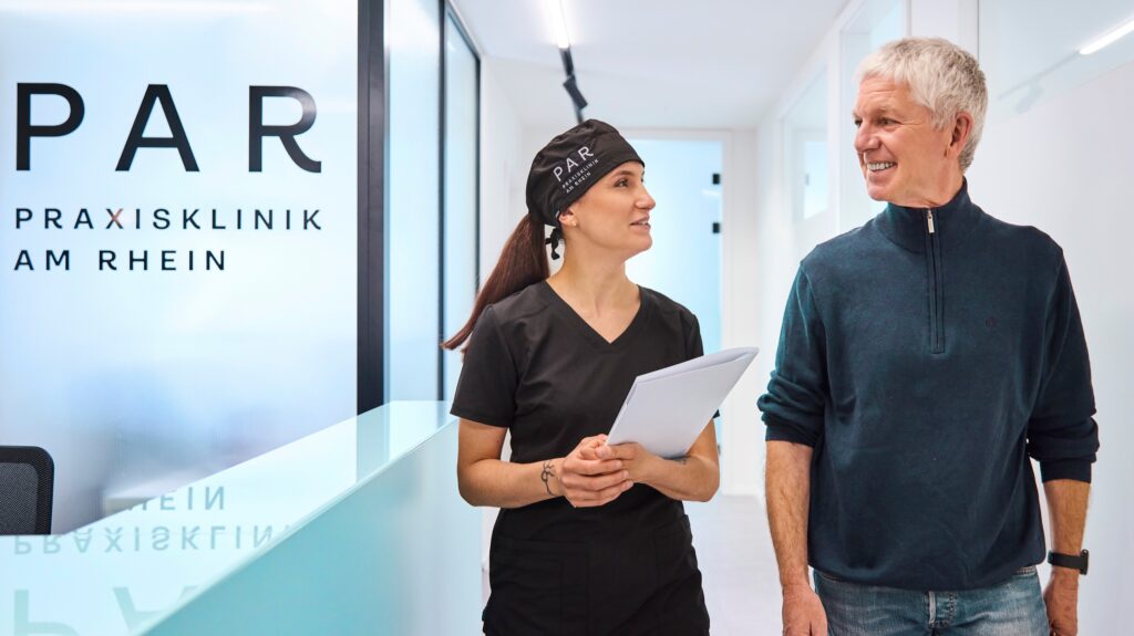 Zahnmedizinische Fachangestellte und Patient gehen durch den Flur der Praxisklinik am Rhein
