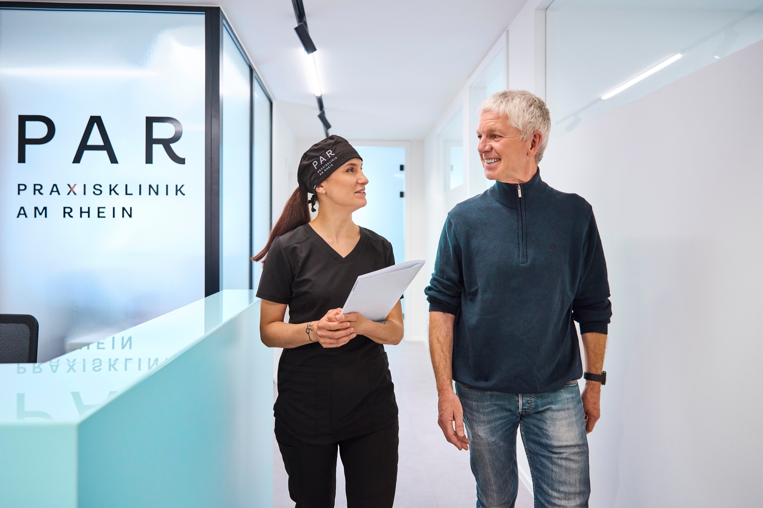 Zahnmedizinische Fachangestellte und Patient gehen durch den Flur der Praxisklinik am Rhein