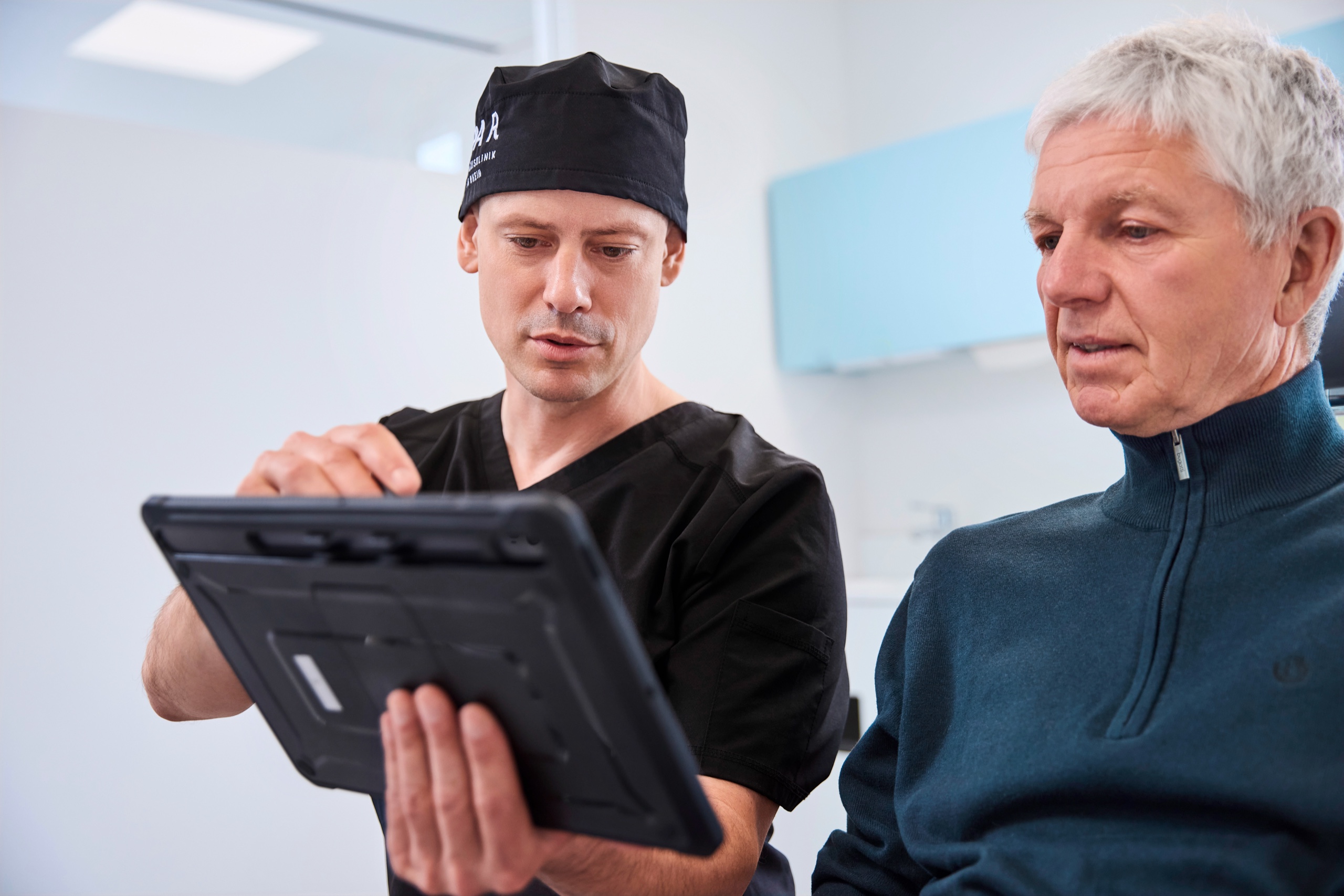 Dr. Romain Doliveux im Beratungsgespräch am Behandlungsplatz zeigt etwas auf einem Tablet