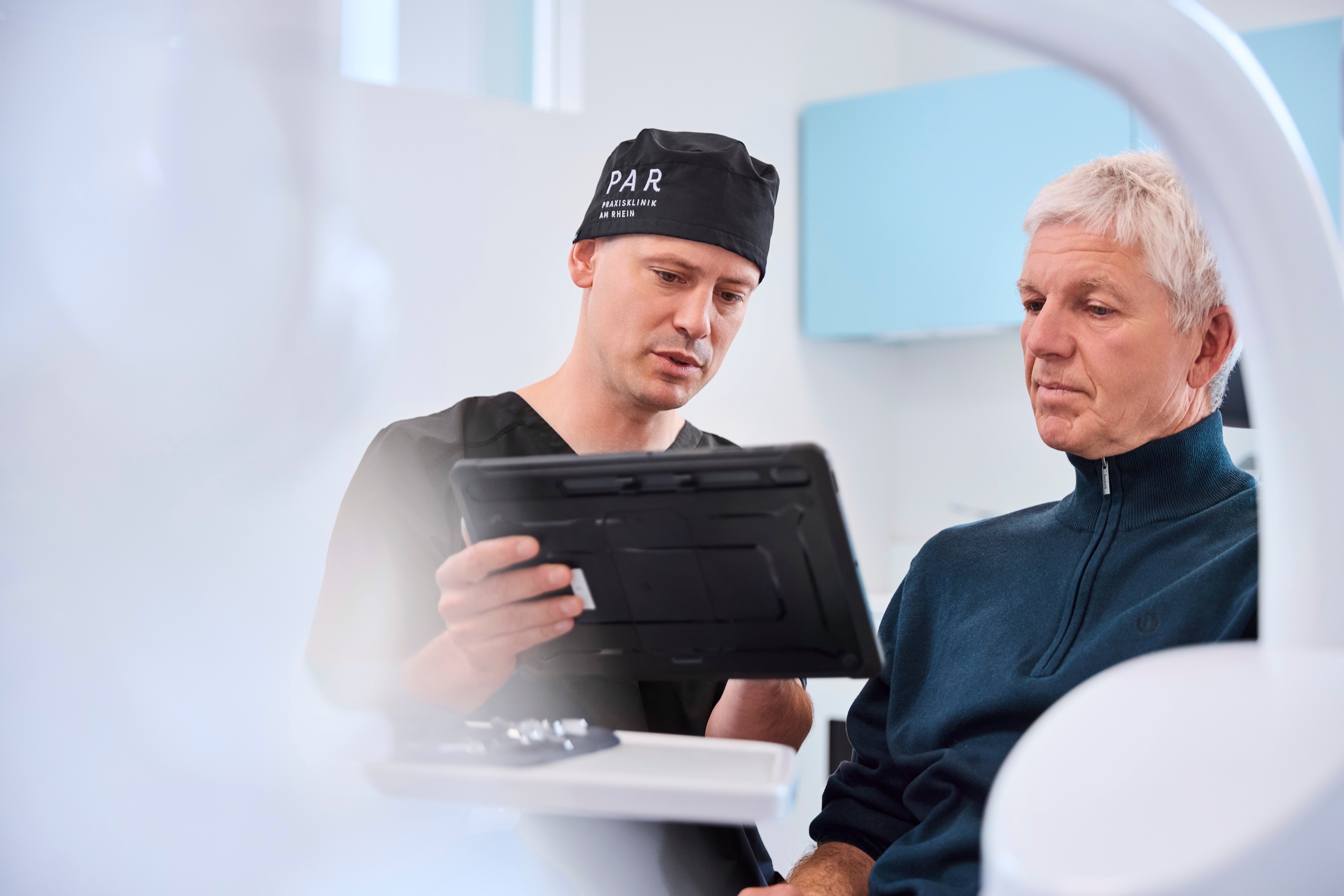 Dr. Romain Doliveux im Beratungsgespräch am Behandlungsplatz zeigt etwas auf einem Tablet
