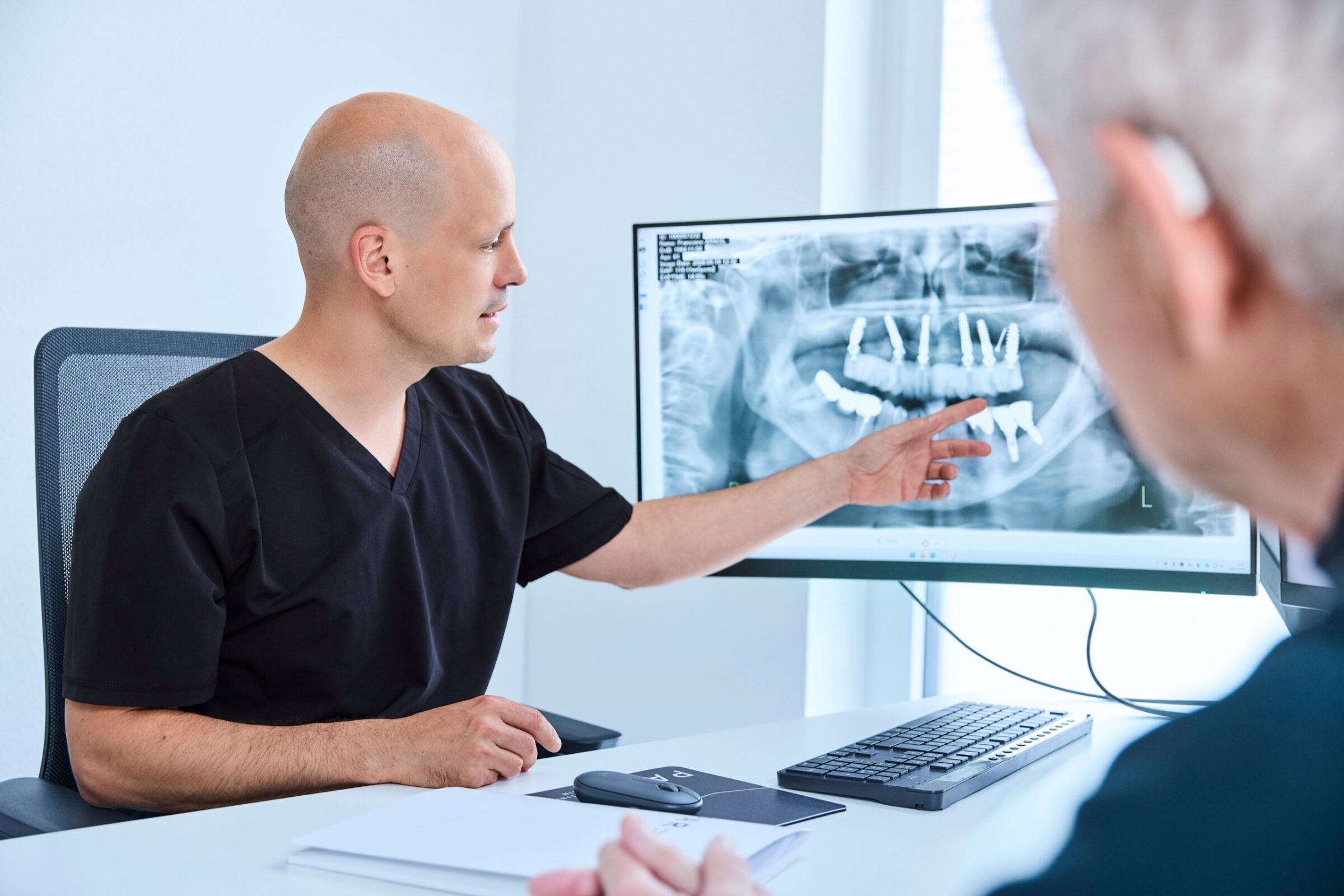 Dr. Romain Doliveux erläutert einem Patienten eine Röntgenaufnahme am Monitor