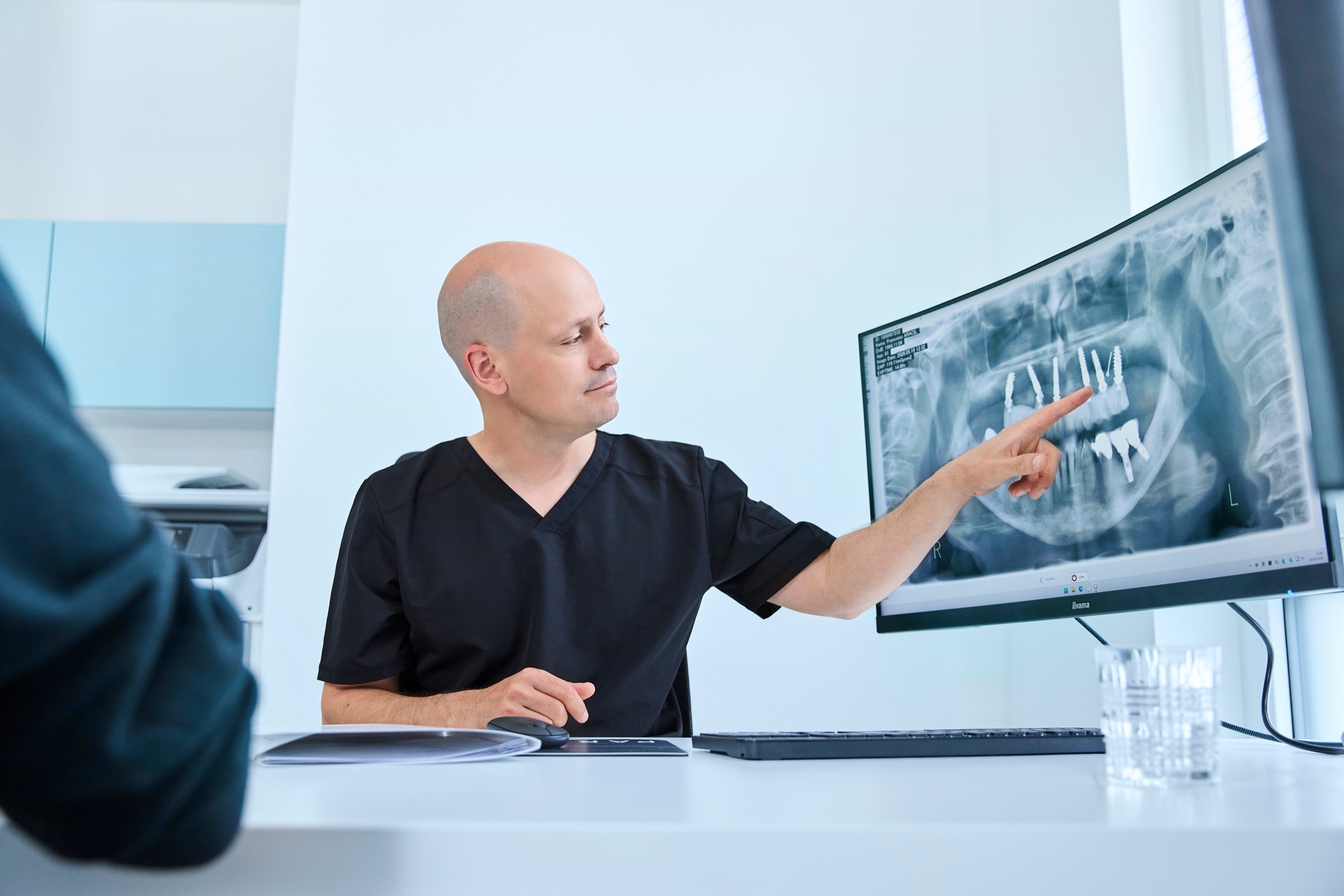 Dr. Romain Doliveux erläutert einem Patienten eine Röntgenaufnahme am Monitor