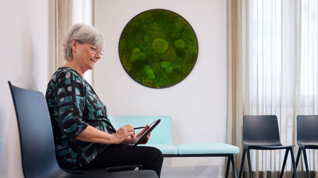 Person im Wartebereich der Praxisklinik am Rhein mit Tablet